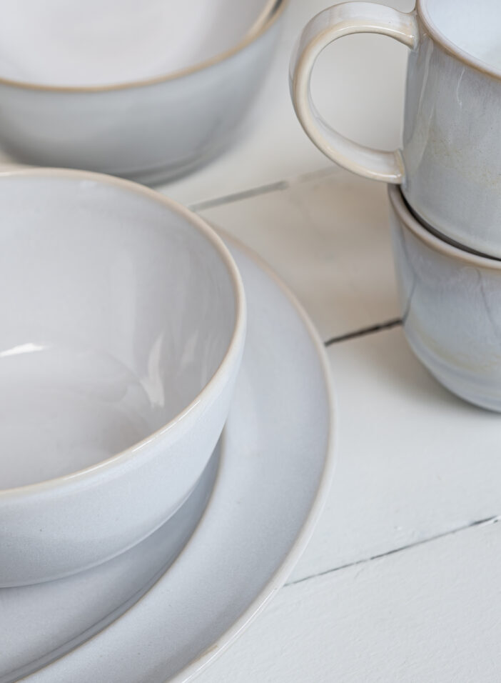 Assiettes, coupelle et mugs en grès sur parquet blanc vue de côté